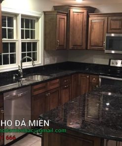 Đá bàn bếp Granite Volga Blue còn được biết đến với tên gọi Xà Cừ Ngọc Trai, là một trong những loại đá granite cao cấp được ưa chuộng trên toàn thế giới. Đá được khai thác chủ yếu tại vùng Golovinske, khu vực Zhitomir, Ukraine. Với màu sắc độc đáo và vẻ đẹp tự nhiên, Volga Blue mang đến vẻ đẹp sang trọng và đẳng cấp cho nhiều hạng mục trang trí nội thất và ngoại thất. Xuất xứ của đá bàn bếp granite Volga Blue Đá Volga Blue được khai thác từ nhiều mỏ khác nhau xung quanh khu vực Golovinske, Zhitomir, Ukraine. Mỗi mỏ đá mang lại những tấm đá với màu sắc và chi tiết vân không hoàn toàn giống nhau, tạo nên sự đa dạng và độc đáo cho từng tấm đá. Đặc điểm của đá bàn bếp granite Volga Blue Volga Blue nổi bật với sự pha trộn giữa màu đen, xanh đậm và xám. Đặc biệt, khi được chiếu sáng, đá ánh lên những hạt khoáng sản lấp lánh, tạo nên hiệu ứng xà cừ ngọc trai vô cùng bắt mắt. Đây là loại đá có hạt khoáng sản to, là một loại khoáng chất anorthosite màu đen, xanh đậm, xám và ánh lên khi gặp ánh sáng. Thành phần khoáng học Đá Volga Blue là một loại anorthosite, chứa nhiều felspat plagioclase (90-100%) cùng với các khoáng chất mafic như pyroxen, ilmenit, magnetit, và olivin. Thành phần khoáng học của đá bao gồm: Plagioclase: 85% Quartz: 7% Pyroxene: 3% Orthoclase: 3% Biotite: 1% Accessories: 1% Thông số kỹ thuật Khả năng hấp thụ nước: 0.07 - 0.09% khối lượng đá. Cường độ nén: 190.70 MPa Khối lượng riêng: 2623 kg/m³ Độ dày: 20mm Bề mặt hoàn thiện Đá Granite Volga Blue có thể được hoàn thiện với các bề mặt sau: Polished (Bóng): Bề mặt đá được đánh bóng, tạo nên độ sáng bóng và phản chiếu ánh sáng đẹp mắt. Honed (Mờ): Bề mặt đá mờ, không bóng, mang lại vẻ đẹp tự nhiên và mộc mạc. Leather (Da): Bề mặt đá có độ nhám nhẹ, tạo cảm giác mềm mại và độc đáo khi chạm vào. Ứng dụng của Đá Bàn Bếp Granite Volga Blue Nhờ vẻ đẹp sang trọng cùng những tính năng ưu việt, đá bàn bếp granite Volga Blue có thể ứng dụng cho cả không gian nội thất và ngoại thất. Nếu biết cách kết hợp với đồ nội và ngoại thất, bạn có thể tạo nên một không gian sống tuyệt đẹp. Ốp bếp Đá Volga Blue là sự lựa chọn hoàn hảo cho bề mặt bếp nhờ màu sắc độc đáo và độ bền cao. Với sự pha trộn của các tông màu đen, xanh đậm và xám, đá tạo ra một không gian bếp hiện đại và tinh tế. Không chỉ mang lại vẻ đẹp sang trọng, bề mặt đá còn dễ dàng vệ sinh, chống thấm nước và chịu được nhiệt độ cao, giúp cho công việc bếp núc trở nên thuận tiện và an toàn hơn. Ốp cầu thang Ứng dụng đá Volga Blue cho cầu thang giúp tạo nên vẻ đẹp mạnh mẽ và bền bỉ. Đặc tính chống mài mòn và khả năng chịu lực tốt của đá granite đảm bảo cho cầu thang có độ bền cao và mang lại cảm giác an toàn cho người sử dụng. Màu sắc và vân đá tinh tế cũng làm tăng thêm sự sang trọng cho không gian sống. Ốp mặt tiền Volga Blue là lựa chọn xuất sắc để ốp mặt tiền nhà, tạo nên điểm nhấn ấn tượng và độc đáo. Màu sắc đá kết hợp với ánh sáng tự nhiên tạo ra hiệu ứng thị giác tuyệt đẹp, thu hút ánh nhìn từ mọi góc độ. Bề mặt đá bền vững với thời gian, giúp mặt tiền ngôi nhà luôn giữ được vẻ đẹp nguyên bản, bất chấp các tác động của thời tiết và môi trường. Ốp tường ngoại thất Với khả năng chống chịu thời tiết và độ bền vượt trội, đá bàn bếp granite Volga Blue cũng được ứng dụng rộng rãi trong các hạng mục ngoại thất. Đá còn giữ được màu sắc và độ bóng lâu dài. Vì vậy, đây là lựa chọn lý tưởng để tạo ra một bức tường ngoại thất đẹp mắt và bền vững, giúp nâng cao giá trị thẩm mỹ và bảo vệ công trình khỏi các tác động xấu từ môi trường. Nếu có điều kiện, bạn có thể sử dụng đá Volga Blue để lát sân vườn mang lại vẻ đẹp tự nhiên và sang trọng cho không gian ngoài trời. Đá granite với độ bền cao, khả năng chống trượt và dễ dàng vệ sinh, giúp sân vườn luôn sạch sẽ và an toàn cho người sử dụng. Màu sắc và hoa văn đặc biệt của đá Volga Blue tạo nên một không gian sân vườn hài hòa với thiên nhiên, mang lại cảm giác thư thái và dễ chịu. Đá Granite Volga Blue (Xà Cừ Ngọc Trai) là lựa chọn hoàn hảo cho cả nội thất và ngoại thất nhờ vào vẻ đẹp độc đáo, độ bền cao và tính năng ưu việt. Từ bề mặt bếp, cầu thang, mặt tiền nhà đến tường ngoại thất và sân vườn, Volga Blue mang lại sự tiện lợi và bền vững cho các công trình kiến trúc. Lưu ý khi sử dụng Do đặc tính dễ vỡ của đá Volga Blue, khi sử dụng chúng ta cần phải gia cố lại bằng tấm nhựa hoặc sợi thủy tinh để đảm bảo độ bền và an toàn của đá. Đặc biệt, khi sử dụng cho các dự án lớn, cần đảm bảo các tấm đá đều được khai thác từ cùng một mỏ để đảm bảo tính đồng nhất về màu sắc và đường vân. Đá Granite Volga Blue (Xà Cừ Ngọc Trai) là lựa chọn lý tưởng cho những ai yêu thích vẻ đẹp tự nhiên và sự sang trọng. Với màu sắc độc đáo, khả năng chống chịu tốt và đa dạng ứng dụng, Volga Blue chắc chắn sẽ mang lại sự hài lòng cho mọi khách hàng. Để tìm hiểu thêm về đá bàn bếp granite Volga Blue, hãy liên hệ với Tổng Kho Đá Miền Bắc. Chúng tôi sẽ tư vấn chi tiết và báo giá tốt nhất cho sản phẩm đá Granite Volga Blue.